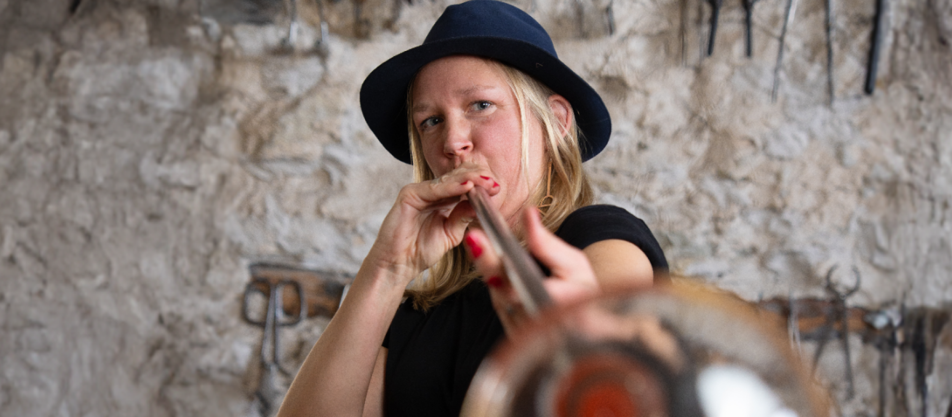 Glasblåsaren Jennie Jessen Jennie Jessen iklädd en hatt blåser ett glas mot kameran
