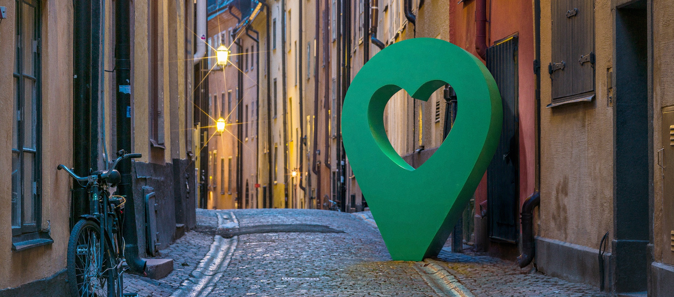 Gamla stan med hjärtpunktmarkör Vacker gata i Gamla stan, Stockholm, med en stor grön hjärtformad punktmarkör längs den kullerstensbelagda vägen.