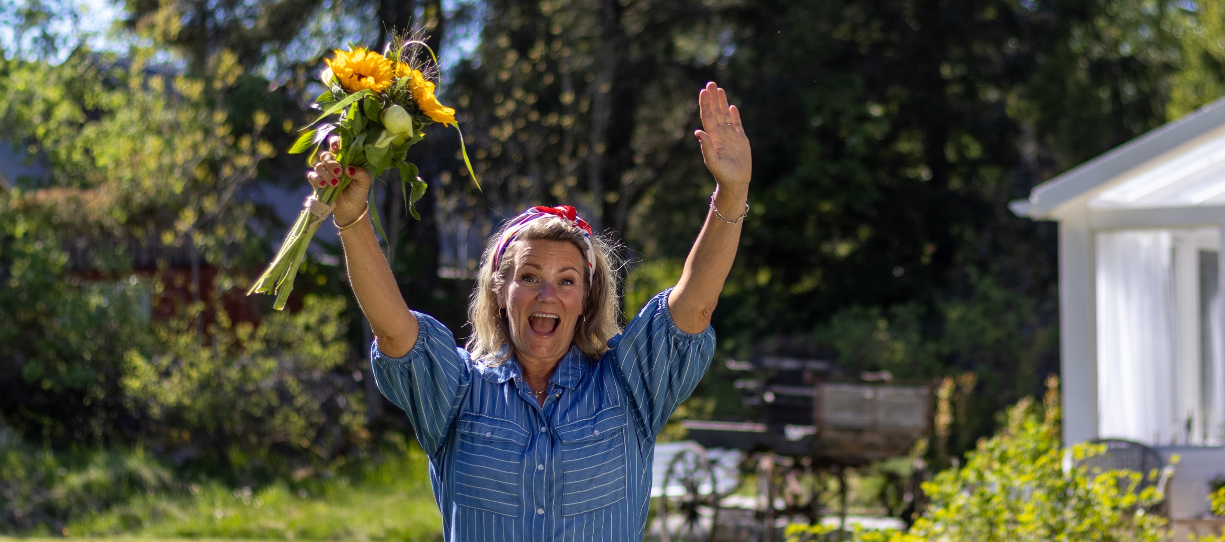 Karin Almström Karin Almström står i en somrig trädgård och håller upp en bukett med gula blommor