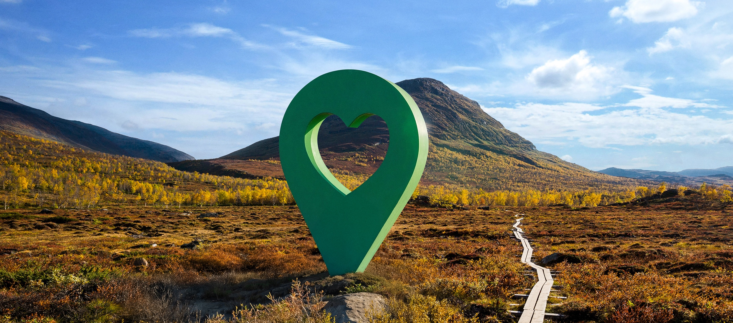 Lyckplatsen i naturen Bild av Lyckplatsen med en stor grön hjärtformad platsmarkering i ett vackert landskap under blå himmel.