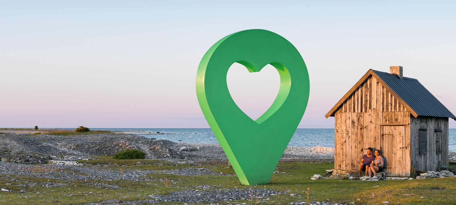 Lyckoplats vid havet En liten stuga vid havet med en grön lyckoplatsmarkering i form av en hjärta placerad framför stugan.