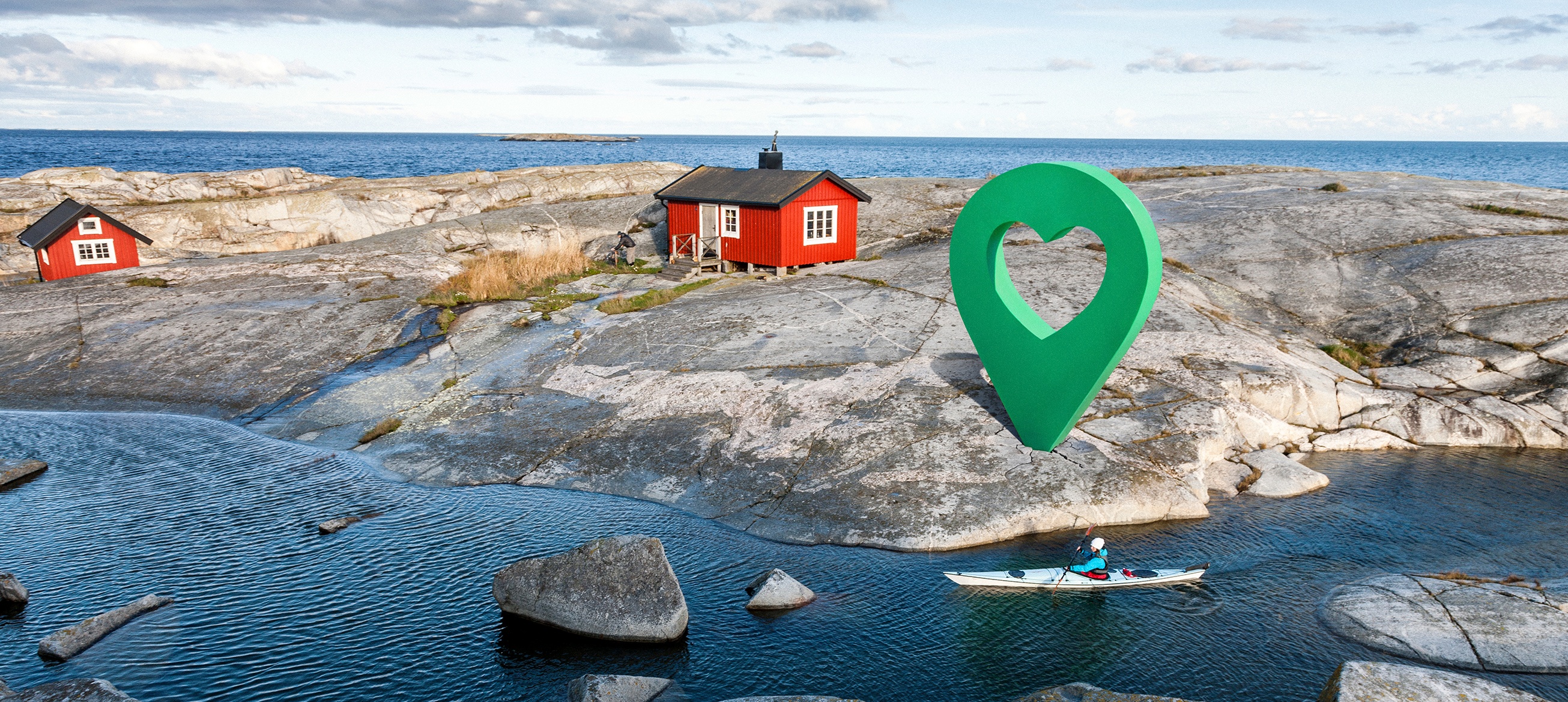 Paddling vid Lyckoplatsen Person paddlar kajak vid klippor med röda stugor och en grön platsmarkör med hjärtsymbol nära Lyckplatsen.