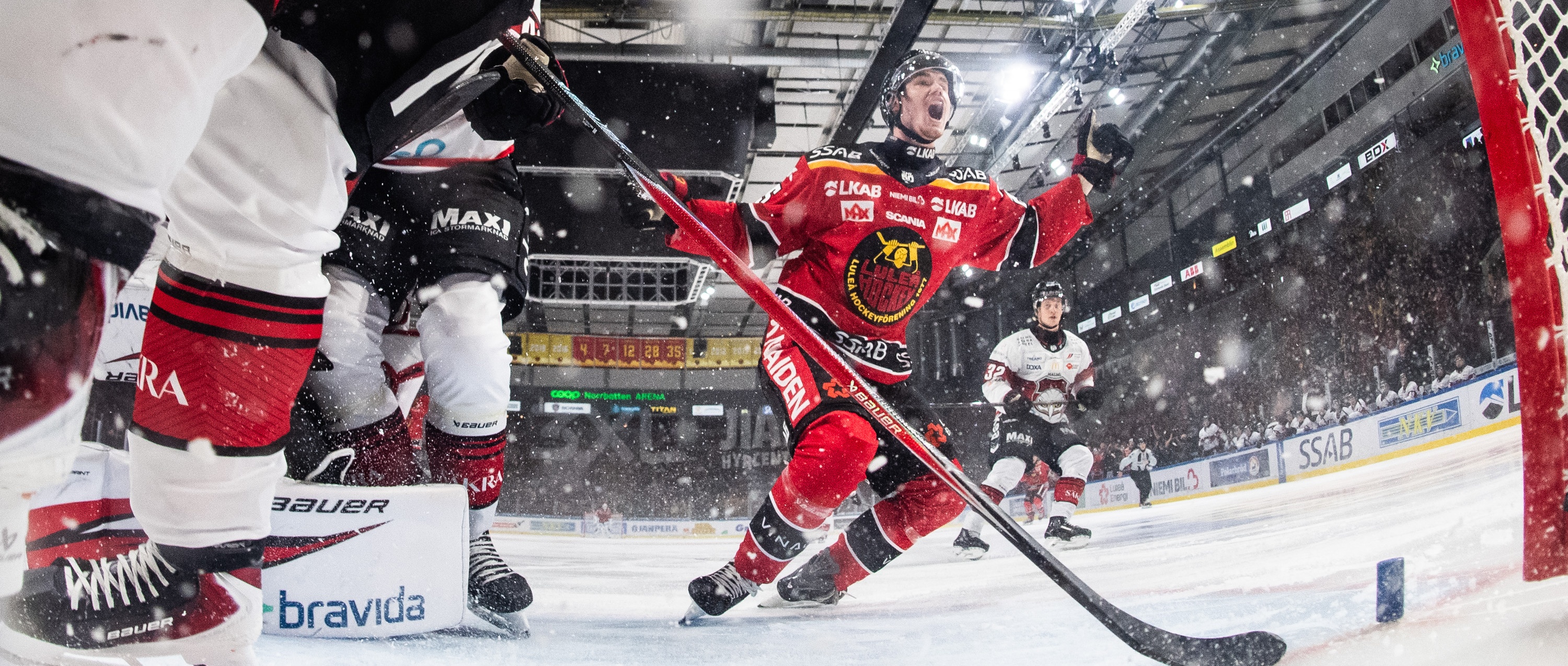 Hockeyspelare firar mål En hockeyspelare i röd dräkt jublar vid målgården efter att ha gjort mål i en ishockeymatch.