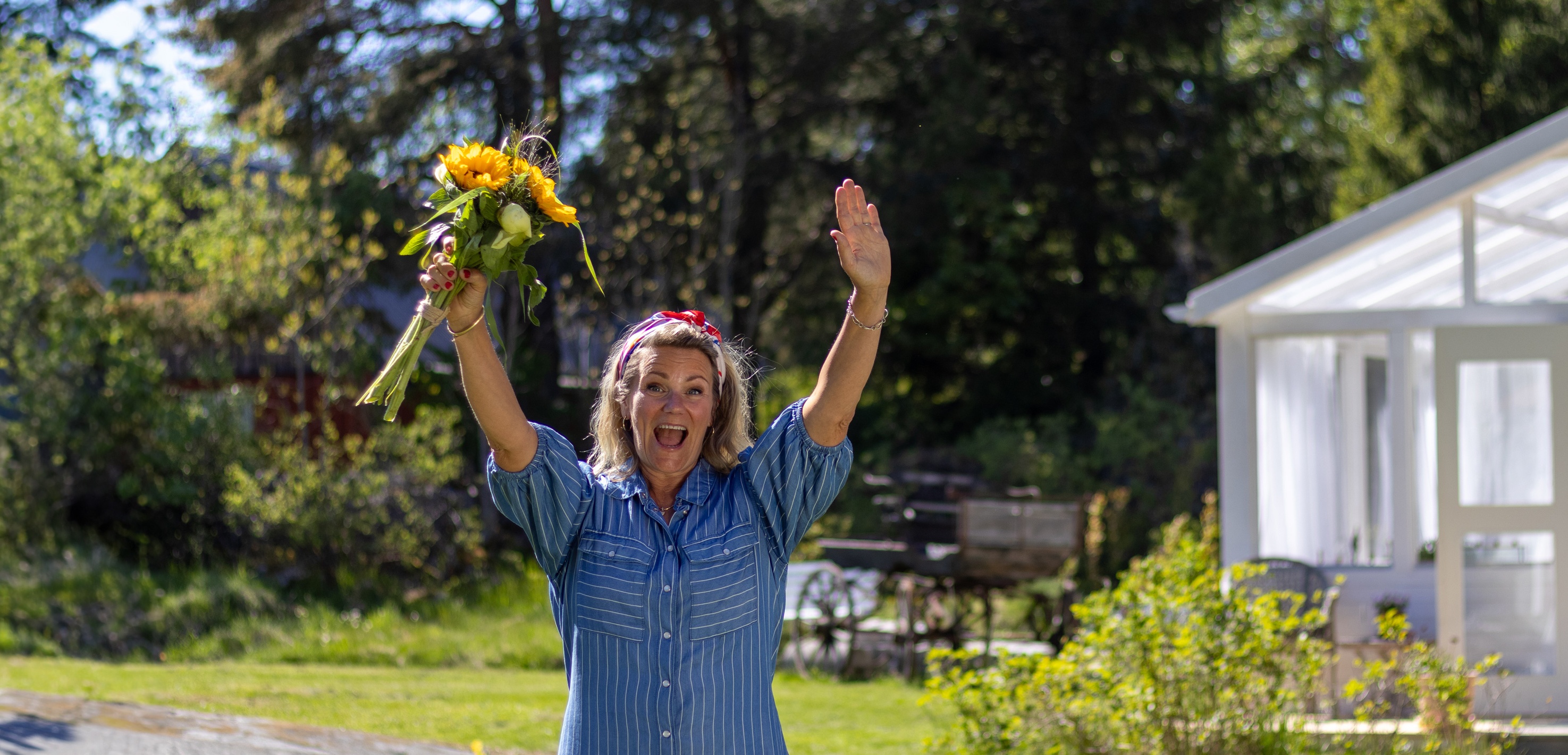 Karin Almström Karin Almström står i en somrig trädgård och håller upp en bukett med gula blommor
