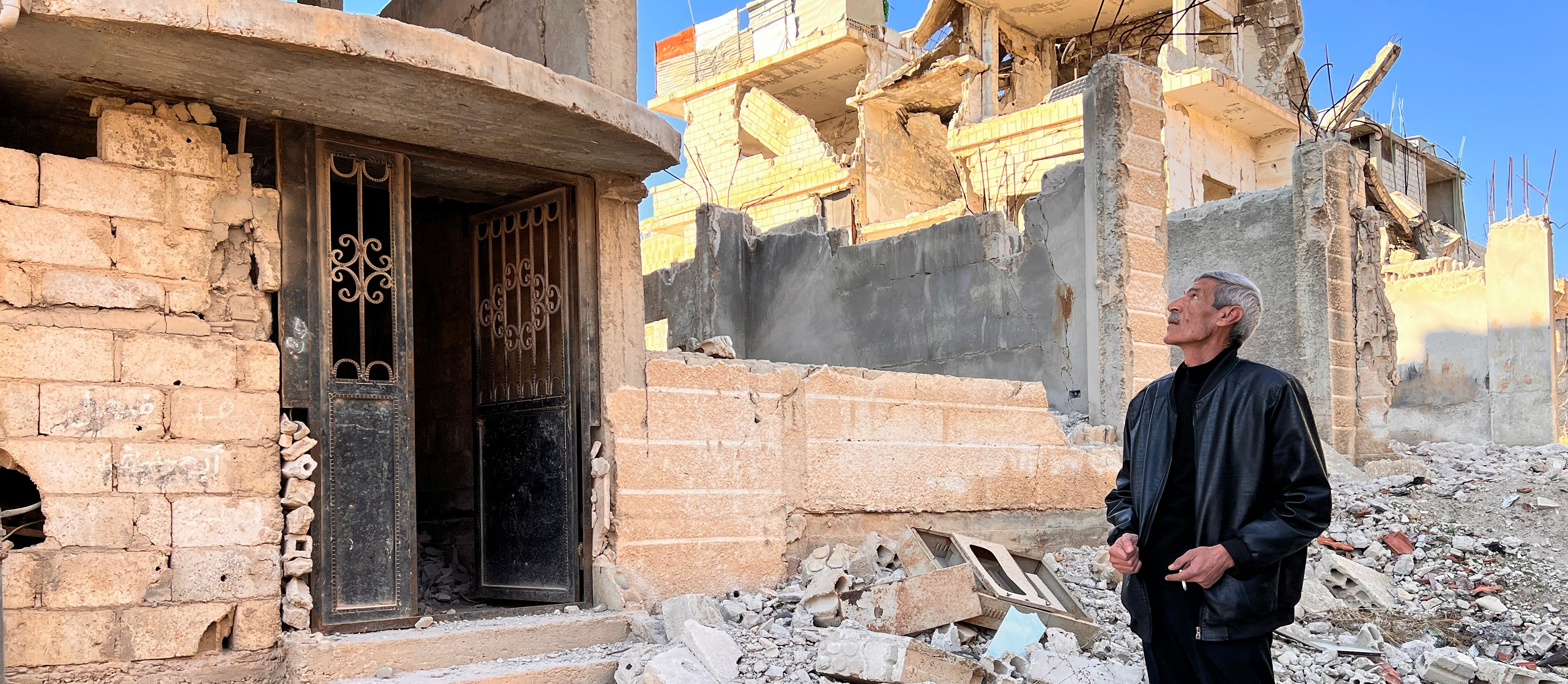 Förstört stadsområde i Syrien En person står bland ruiner i ett förstört stadsområde i Syrien, med trasiga byggnader omkring.