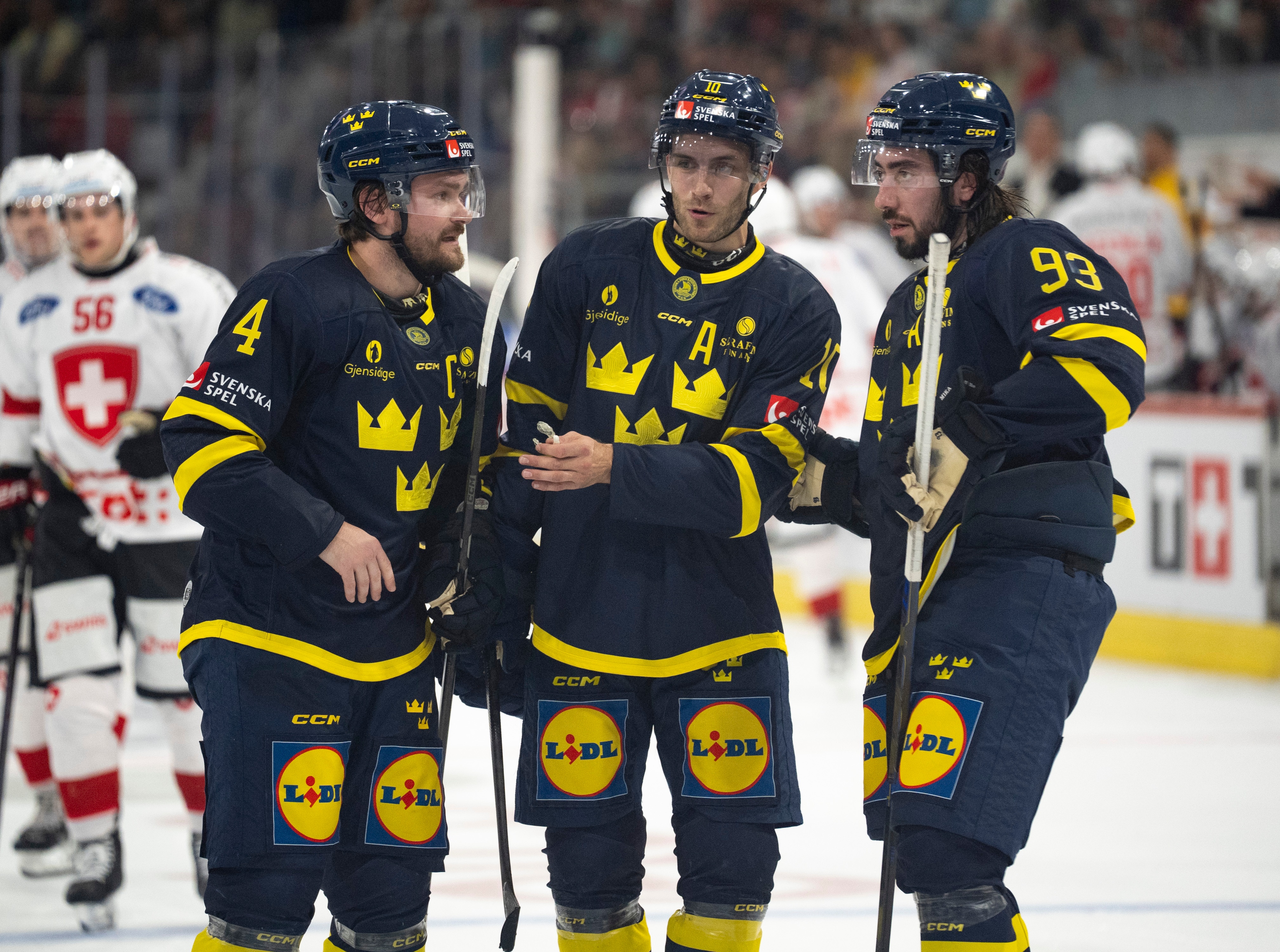 Tre svenska ishockeyspelare i blå och gula landslagsuniformer samt hållet i samtal på isen.