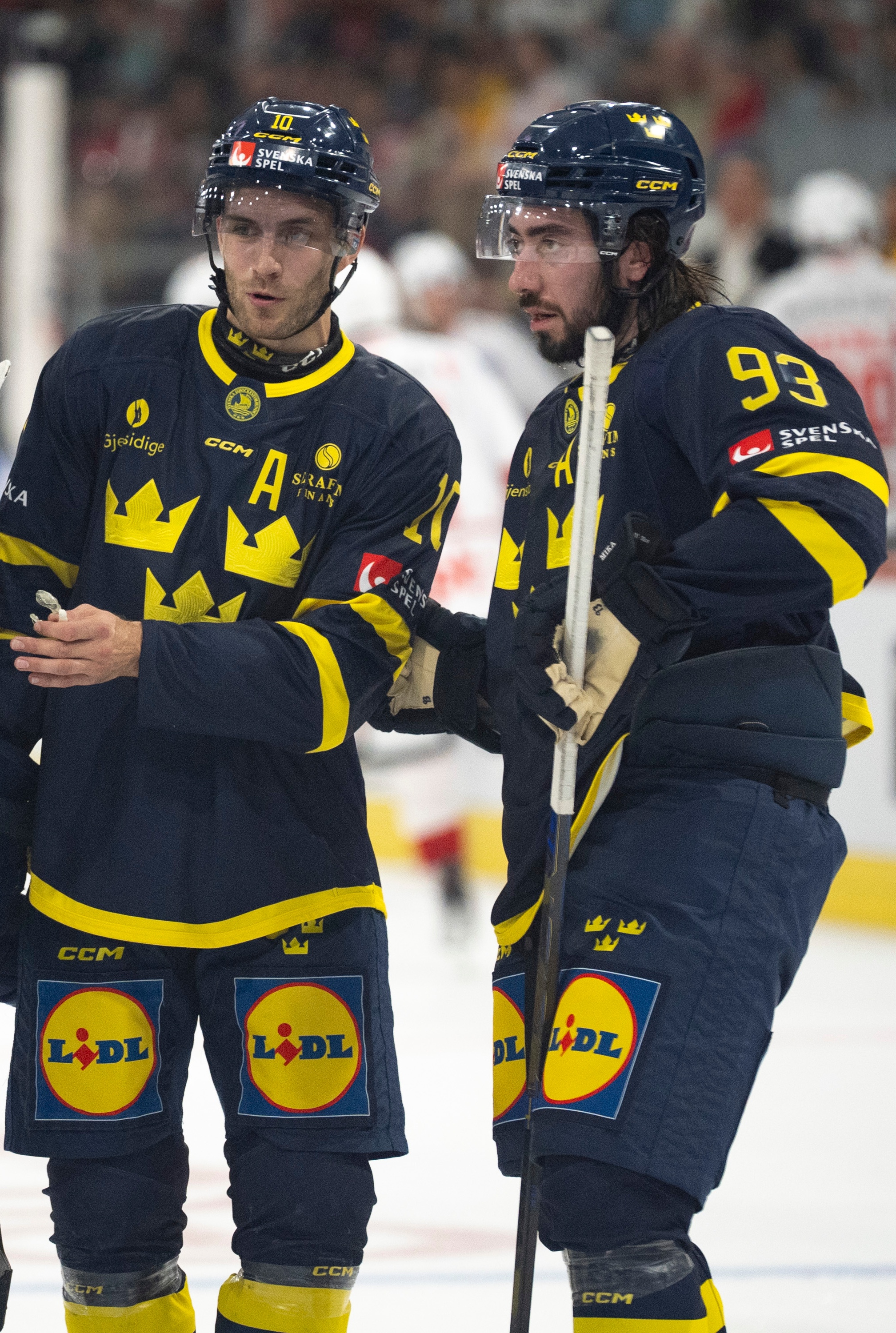 Tre svenska ishockeyspelare i blå och gula landslagsuniformer samt hållet i samtal på isen.