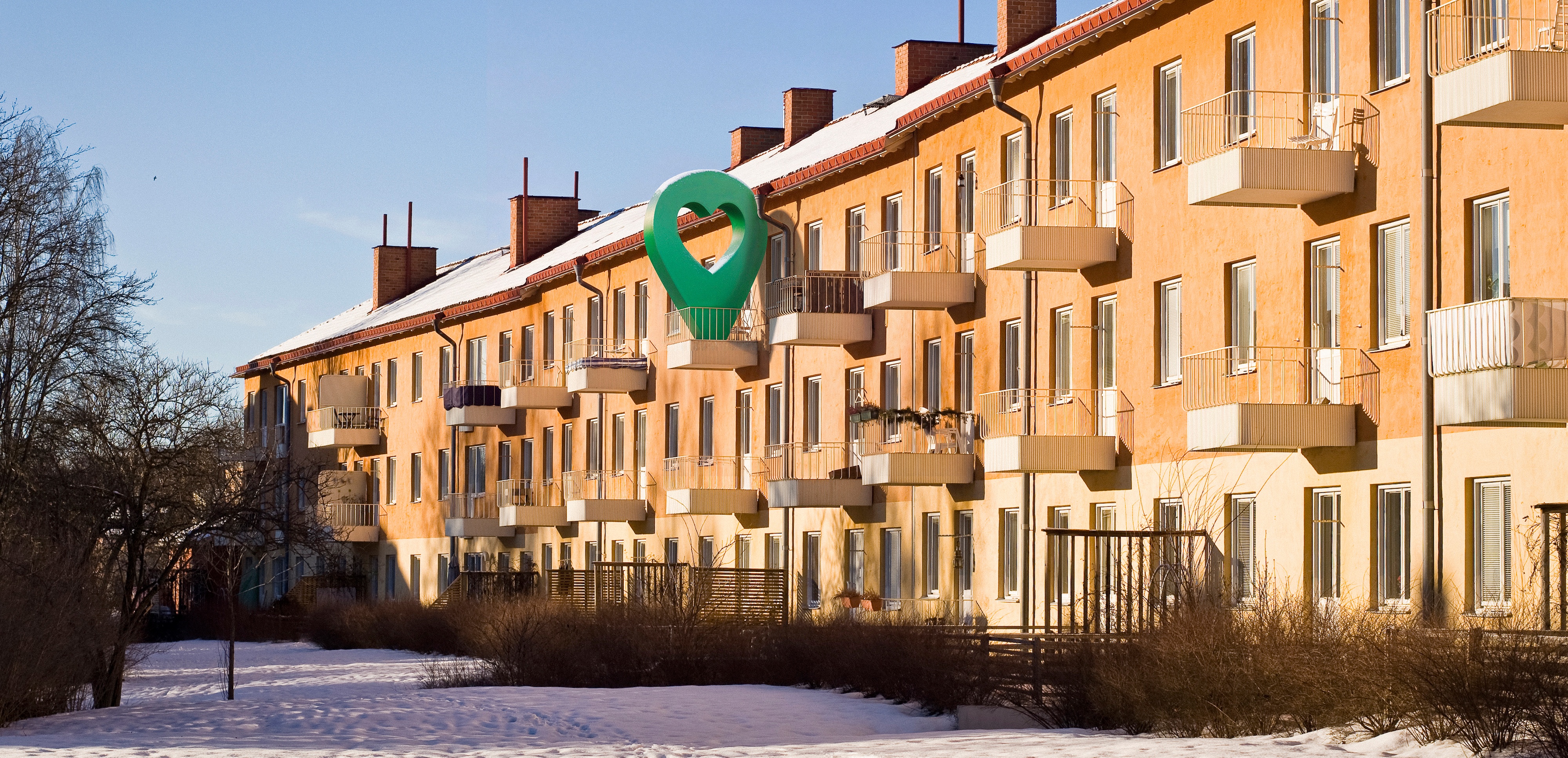 Lägenhetshus i vintermiljö med snöklädd mark och klarblå himmel.