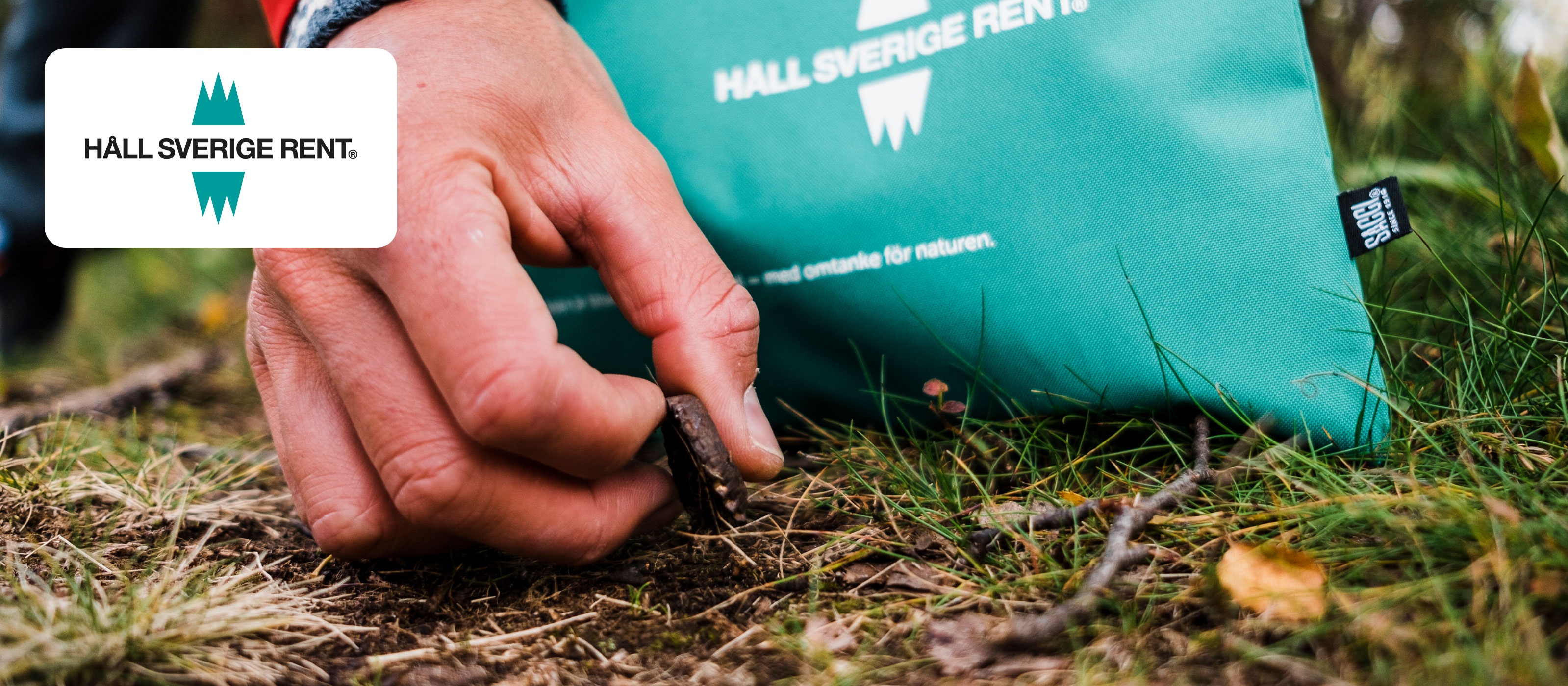 Bild av en hand som plockar skräp från marken med en grön påse märkt 'Håll Sverige Rent'.