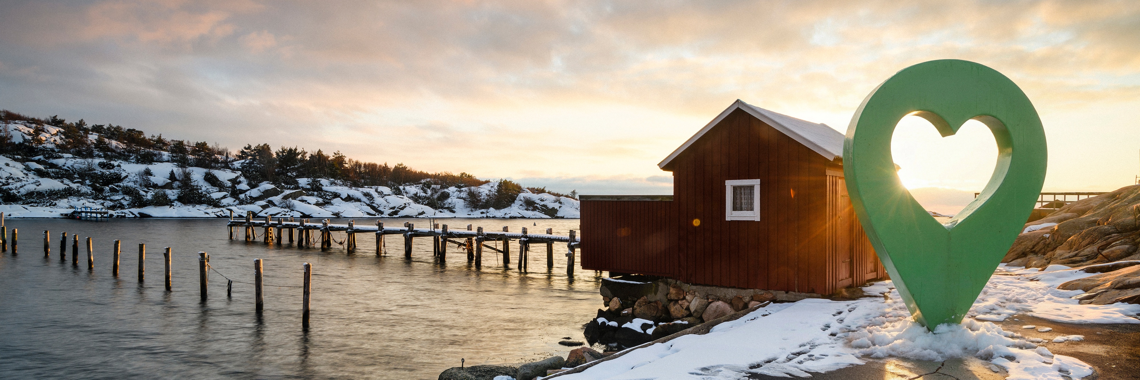 Vinterlandskap med en fiskestuga vid en snötäckt kust och en stor grön platsmarkör med hjärta.