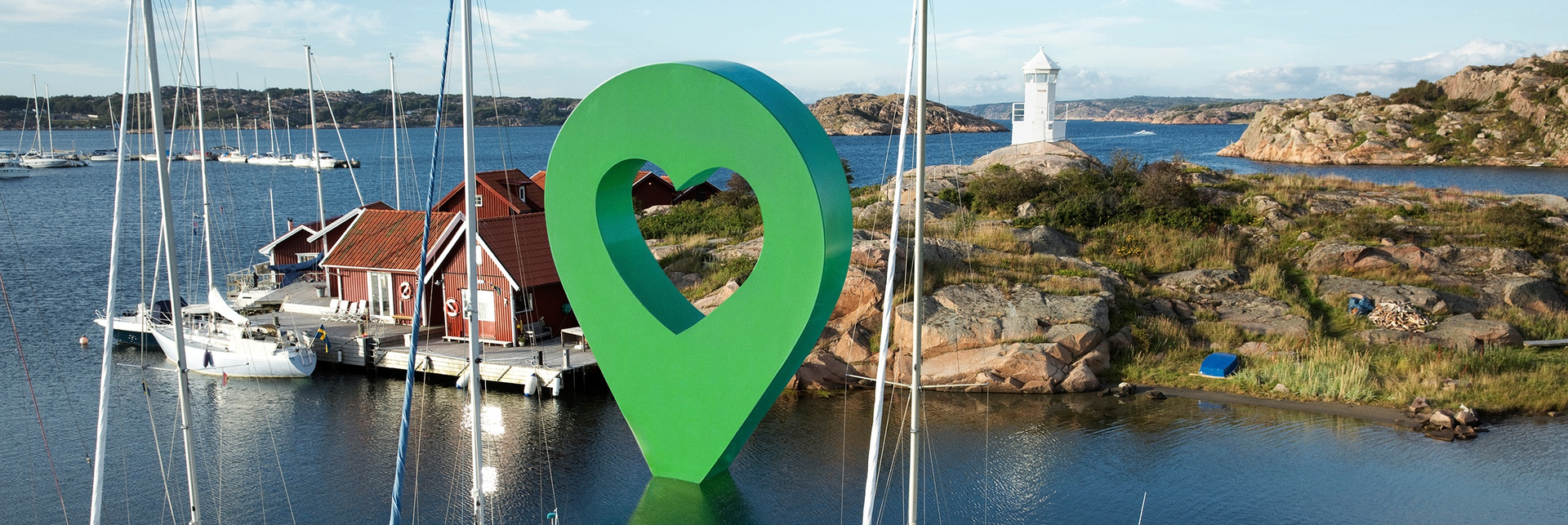 Panoramavy av en svensk småbåtshamn med båtar och hus vid vattnet. En stor Lyckplatsen-pin sitter i viken.