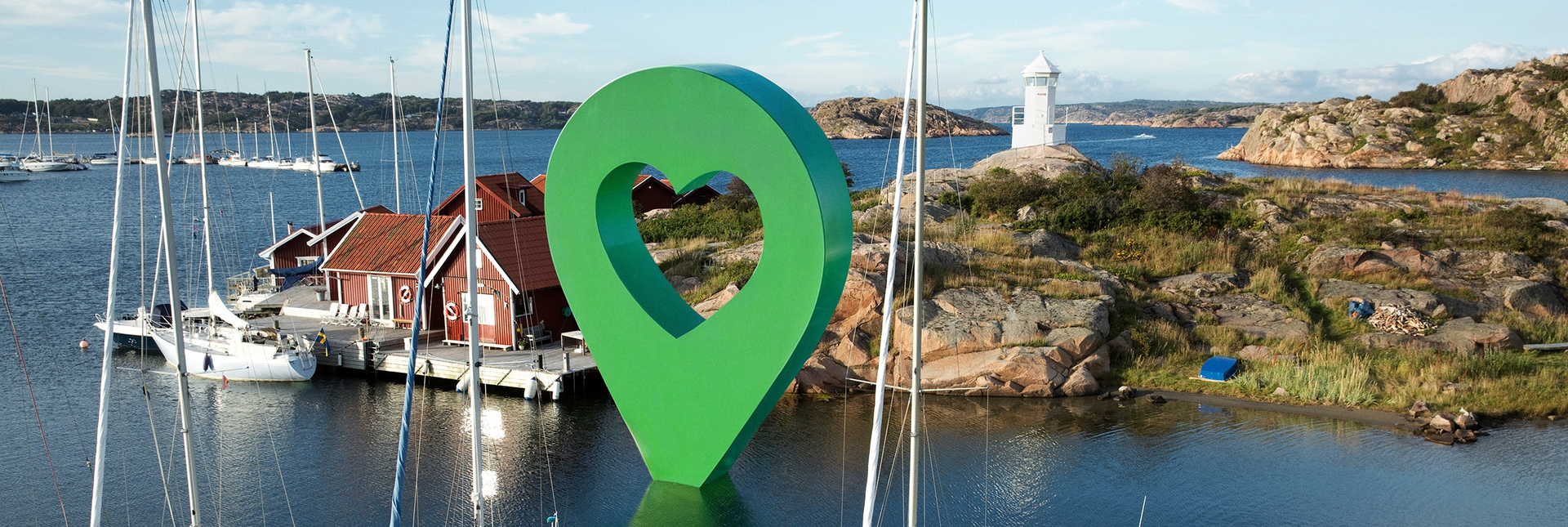 Panoramavy av en svensk marina med båtar och hus vid vattnet. En stor grön Lyckoplatsen-pin synlig i mitten.