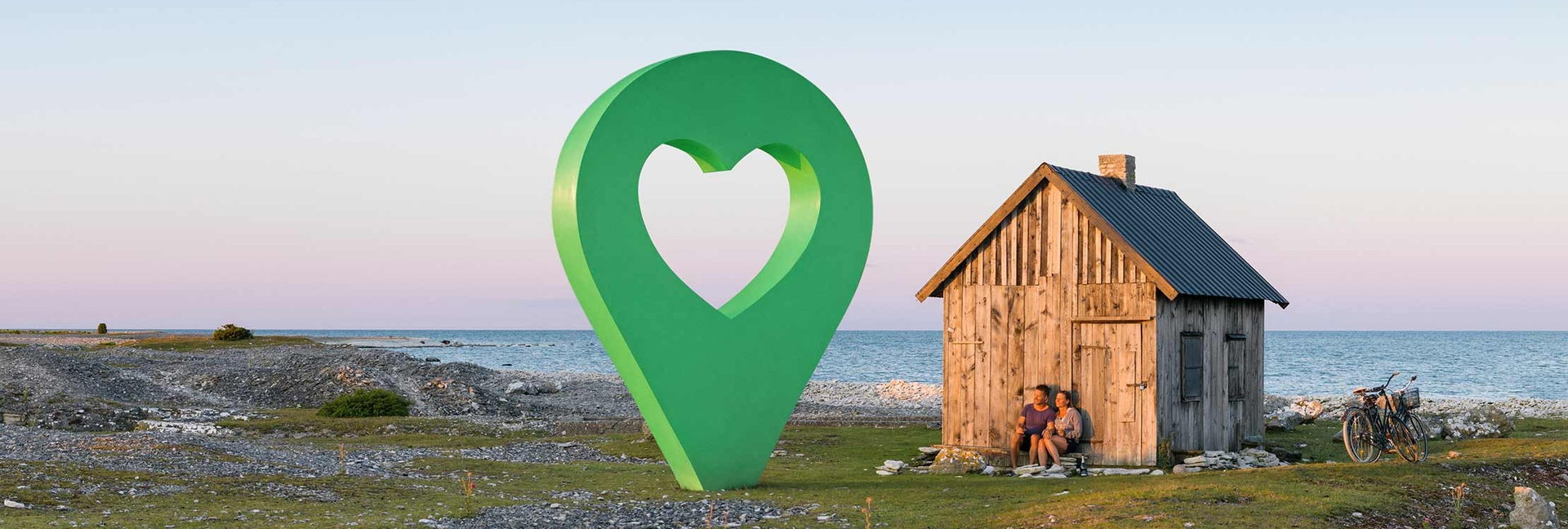 En liten stuga vid havet med en grön lyckoplatsmarkering i form av en hjärta placerad framför stugan.