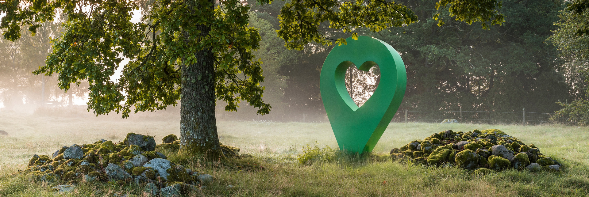 Grön lyckplats-symbol med hjärta mitt i en skog. Symbolen står nära ett träd och en stenig plats.