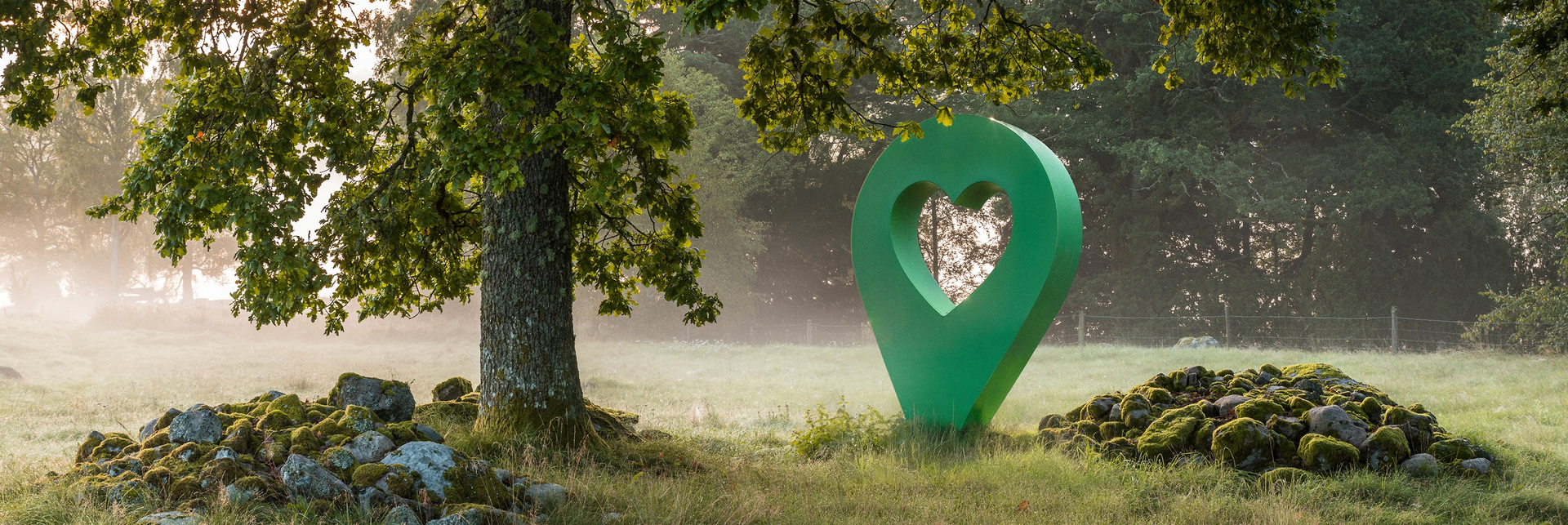Grön lyckplats-symbol med hjärta mitt i en skog. Symbolen står nära ett träd och en stenig plats.