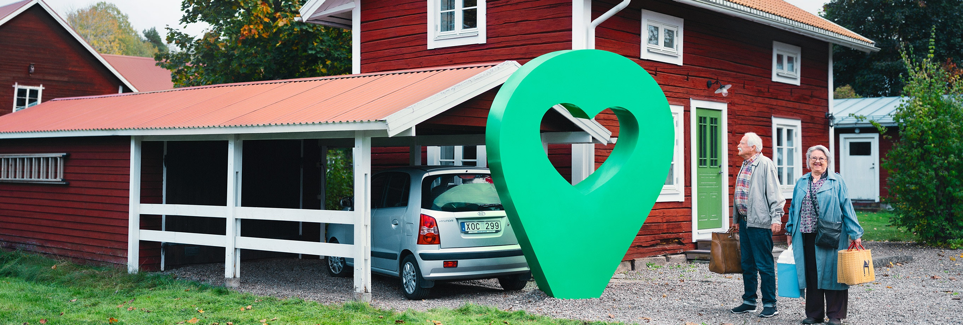 Ett rött sommarhus med carport och två glada personer. En grön pin med hjärta är placerad vid huset.