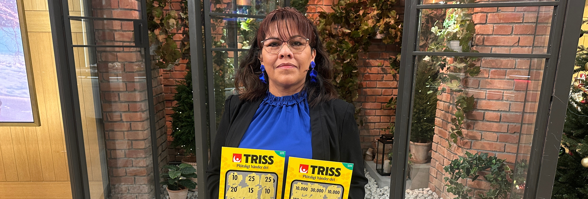 Trissvinnaren Fanny visar upp två vinnande Trisslotter på TV-studio med juldekorationer i bakgrunden.