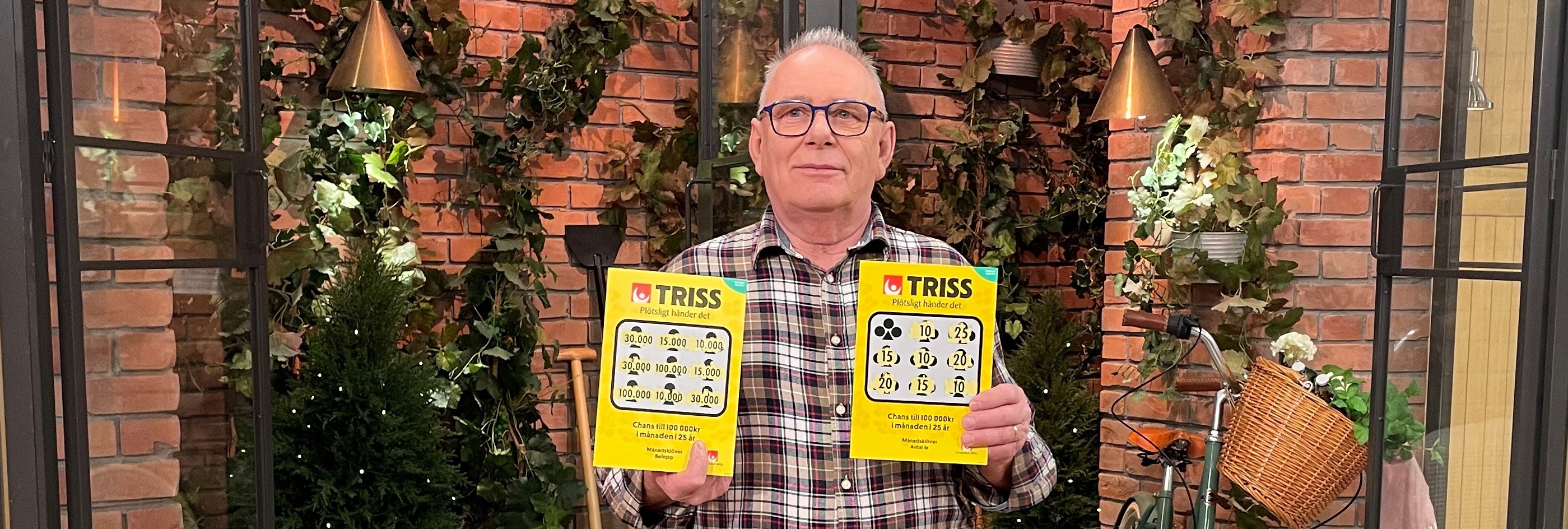 Trissvinnare Bo håller två gula Trisslotter med svart text mot bakgrund av grönska och tegelvägg.