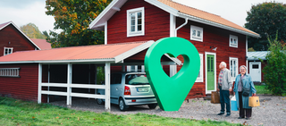 Ett rött sommarhus med carport och två glada personer. En grön pin med hjärta är placerad vid huset.