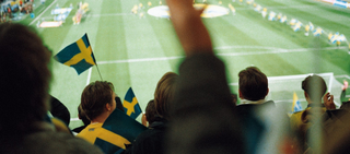 Publik med svenska flaggor på en fotbollsmatch på en stor arena.