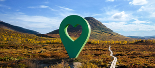 Bild av Lyckplatsen med en stor grön hjärtformad platsmarkering i ett vackert landskap under blå himmel.