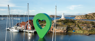 Panoramavy av en svensk småbåtshamn med båtar och hus vid vattnet. En stor Lyckplatsen-pin sitter i viken.