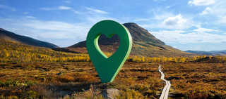 Bild av Lyckplatsen med en stor grön hjärtformad platsmarkering i ett vackert landskap under blå himmel.