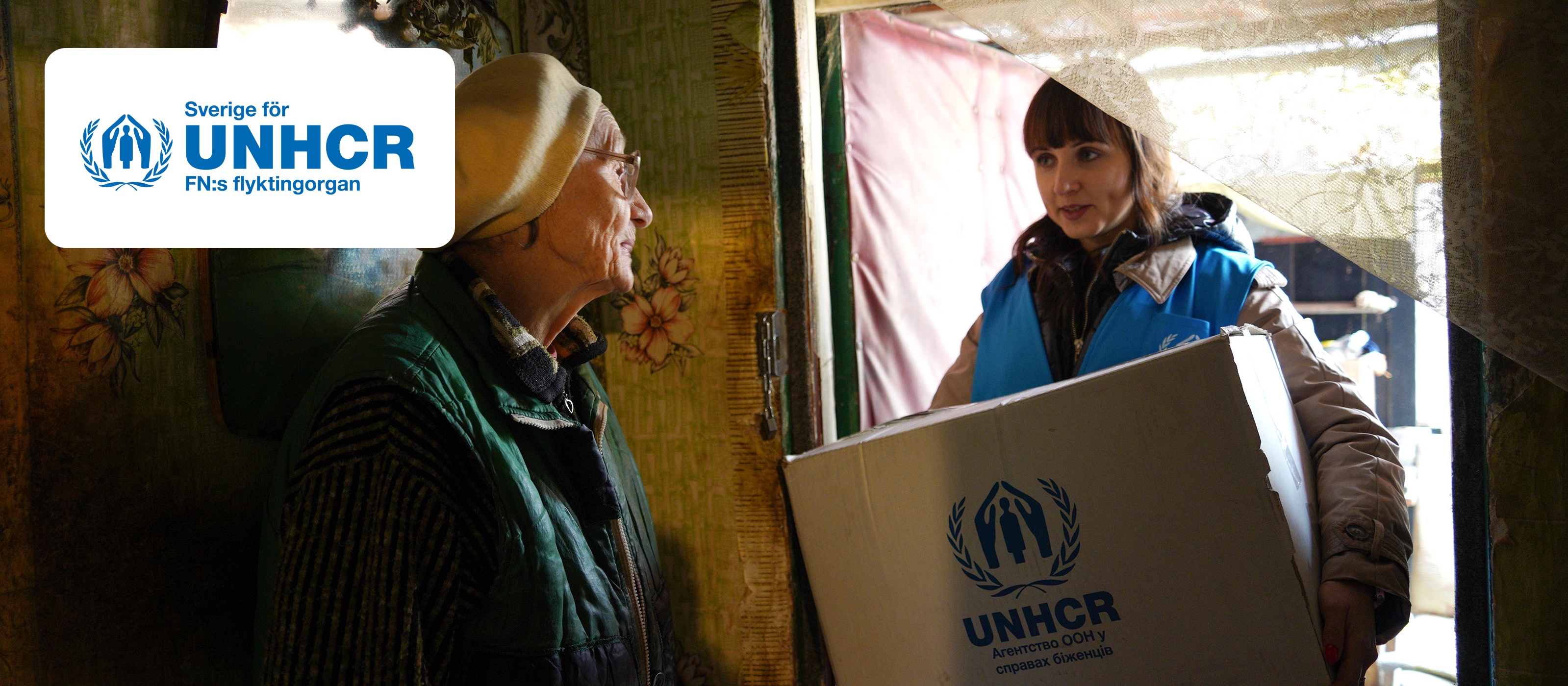UNHCR-anställd som levererar en låda till en äldre person i Ukraina, med logga i hörnet.