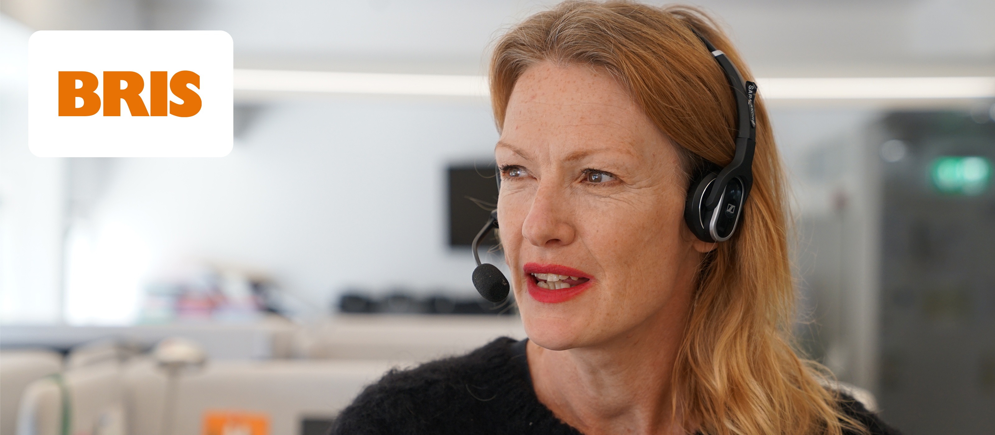 Kvinna med headset vid BRIS-logga i bakgrunden, engagerad arbetsmiljö.