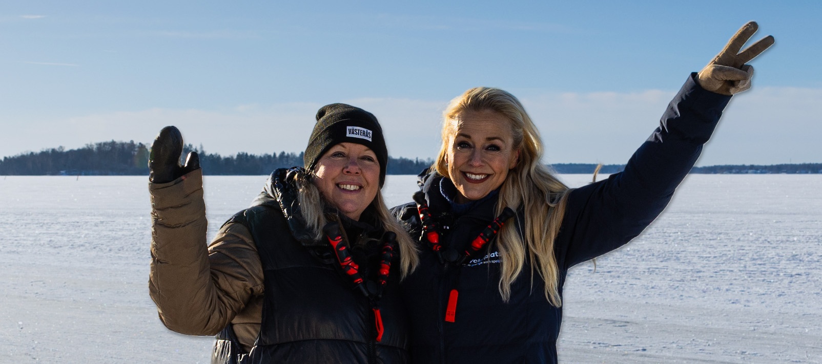 Två glada personer poserar på en frusen sjö med blå himmel i bakgrunden.