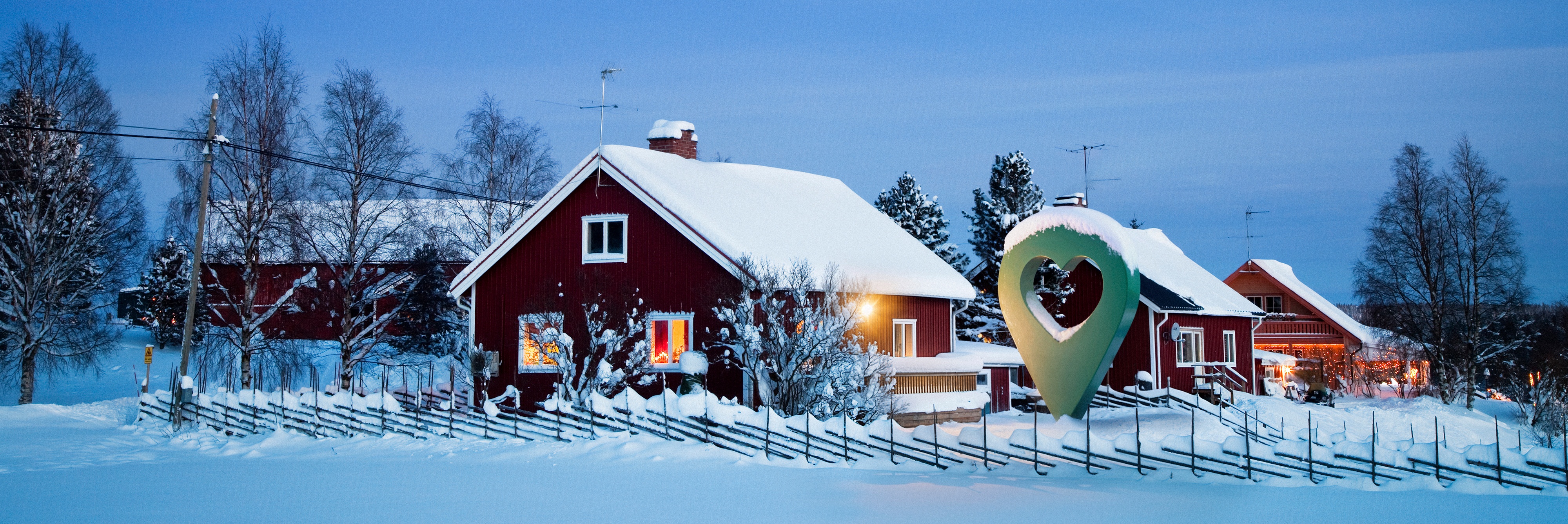 En vintrig landskapsvy med röda hus täckta av snö under en natthimmel och månen synlig.
