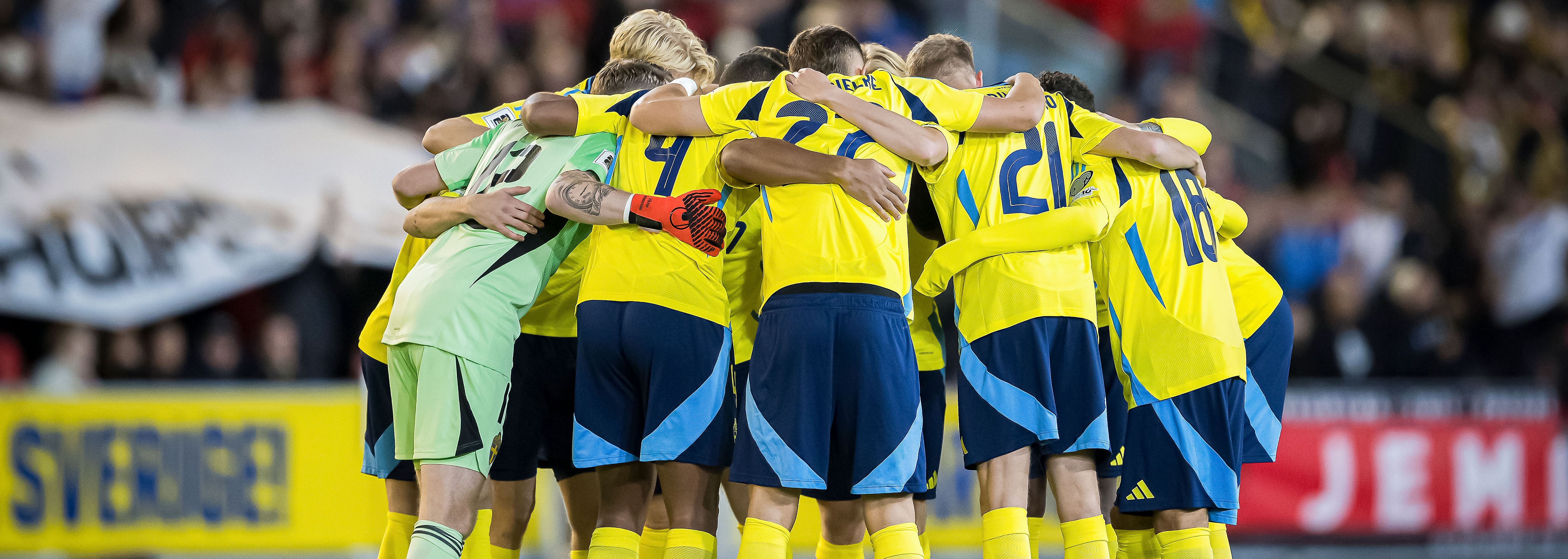 Svenska herrlandslaget i fotboll står i en cirkel och kramar om varandra på fotbollsplanen.