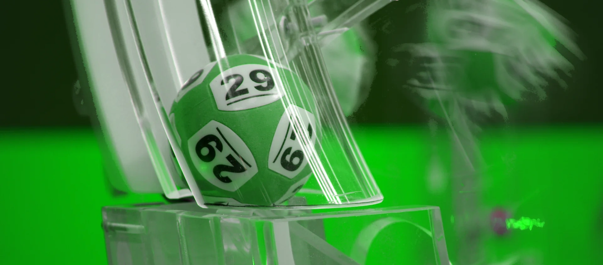 Grön lottoboll i en dragning med nummer 29 synlig i en lottotrumma med grön bakgrund.
