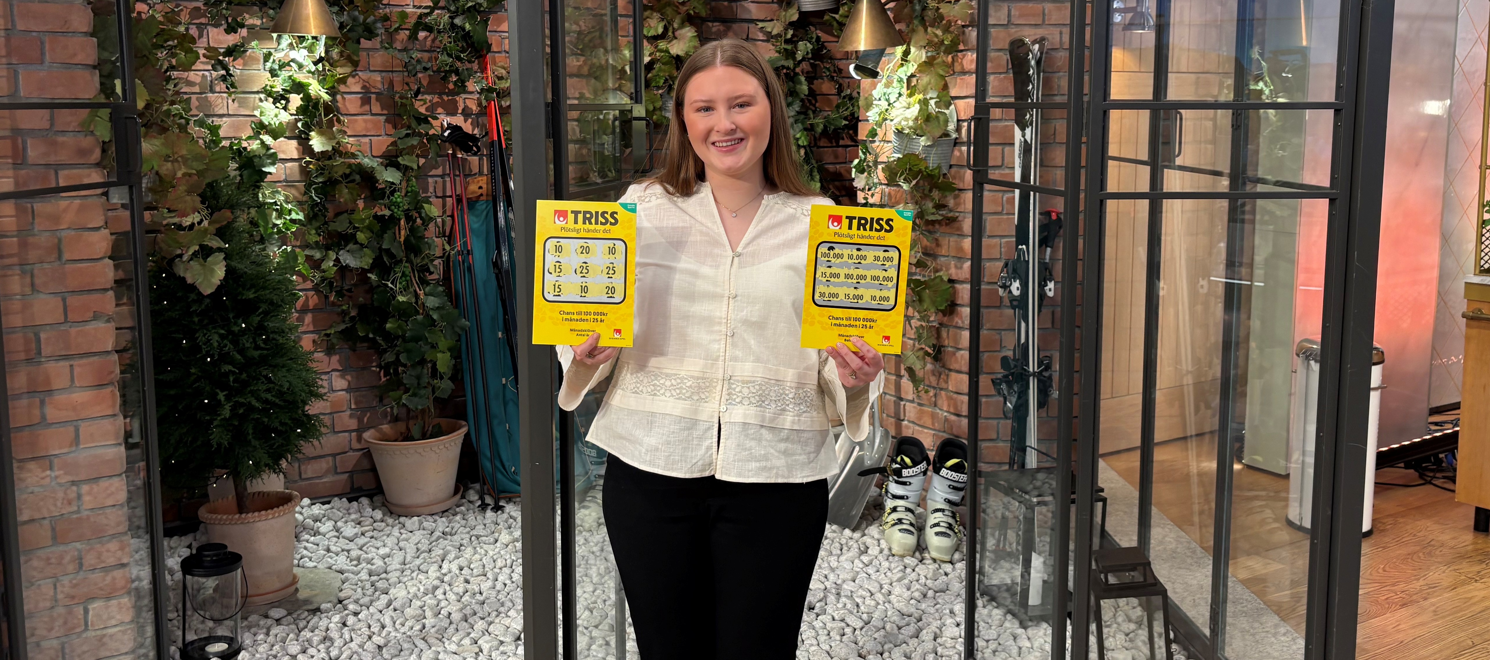Person håller två Trisslotter och står i en inglasad trädgårdsmiljö med växter i bakgrunden.