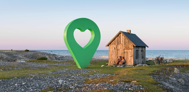 En liten stuga vid havet med en grön lyckoplatsmarkering i form av en hjärta placerad framför stugan.