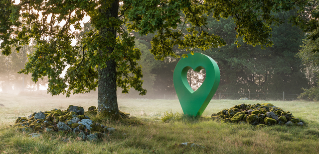 Grön lyckplats-symbol med hjärta mitt i en skog. Symbolen står nära ett träd och en stenig plats.