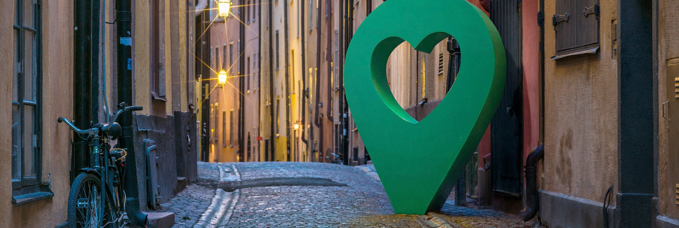 Vacker gata i Gamla stan, Stockholm, med en stor grön hjärtformad punktmarkör längs den kullerstensbelagda vägen.