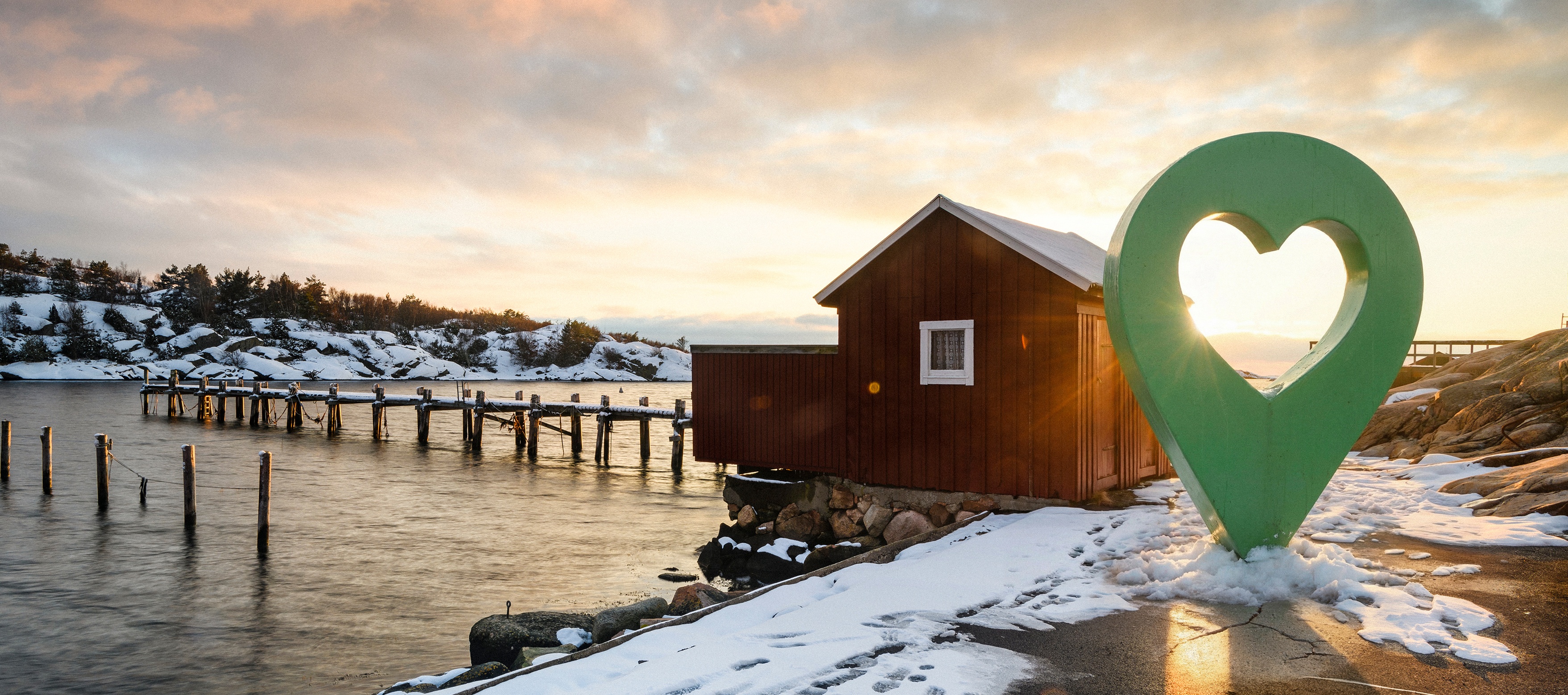 Vinterlandskap med en fiskestuga vid en snötäckt kust och en stor grön platsmarkör med hjärta.