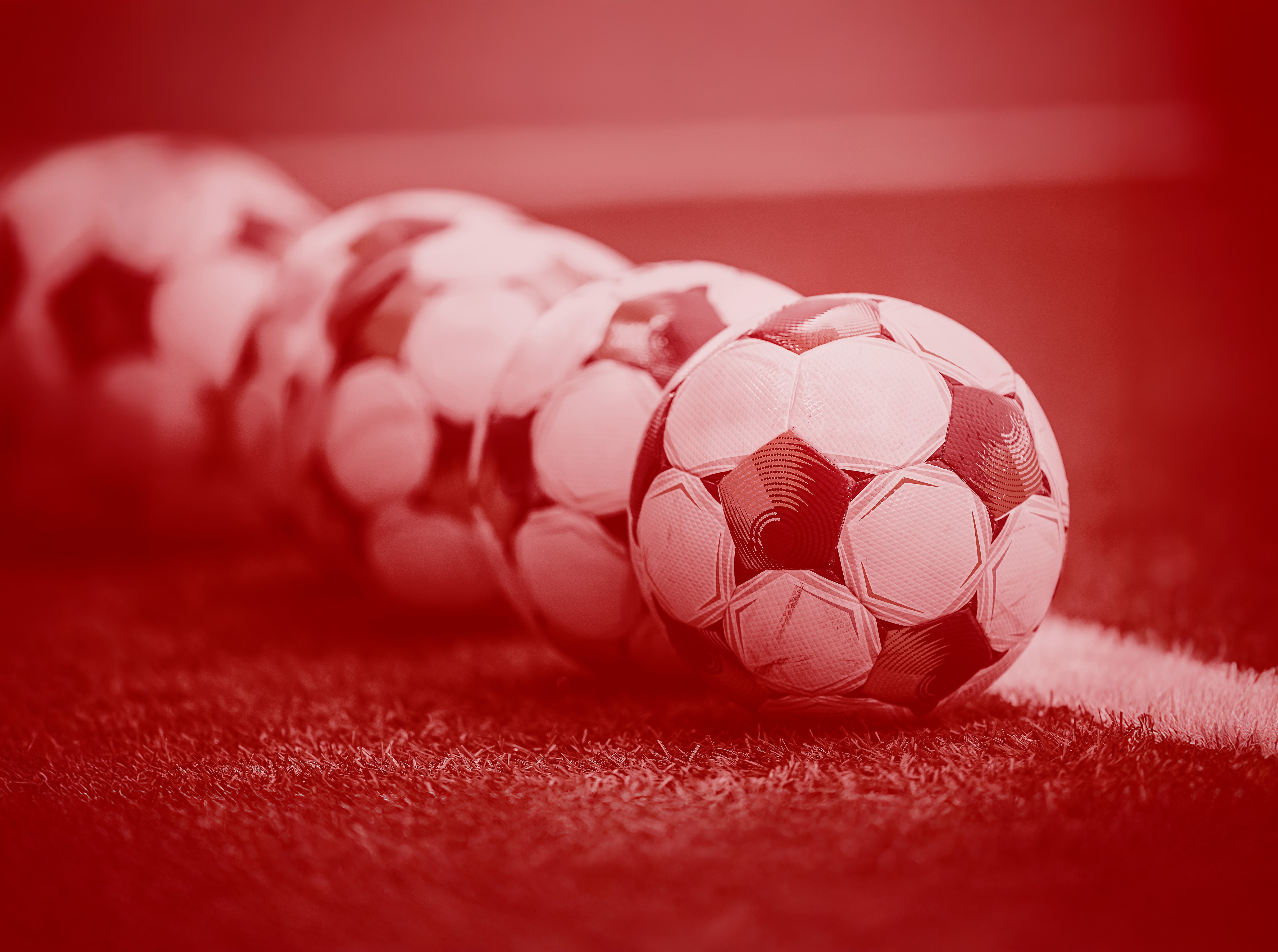 Fyra fotbollar ligger på en gräsmatta. Bilden har en röd ton och är associerad med Oddset Allsvenskan.