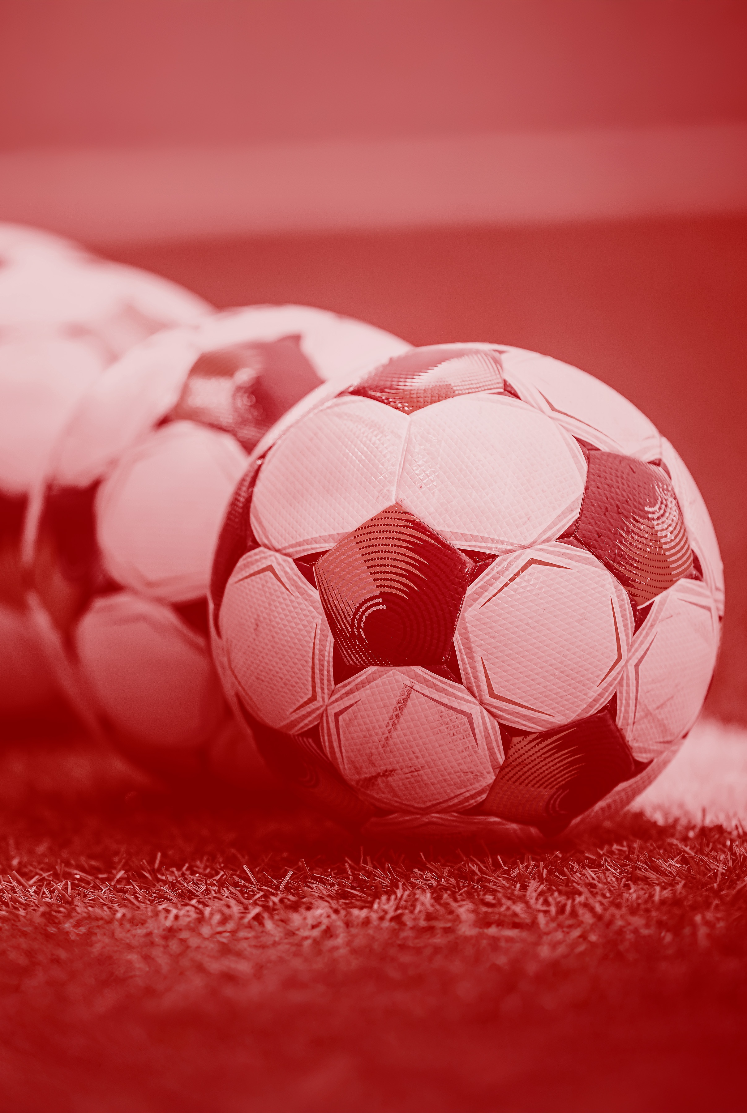 Fyra fotbollar ligger på en gräsmatta. Bilden har en röd ton och är associerad med Oddset Allsvenskan.