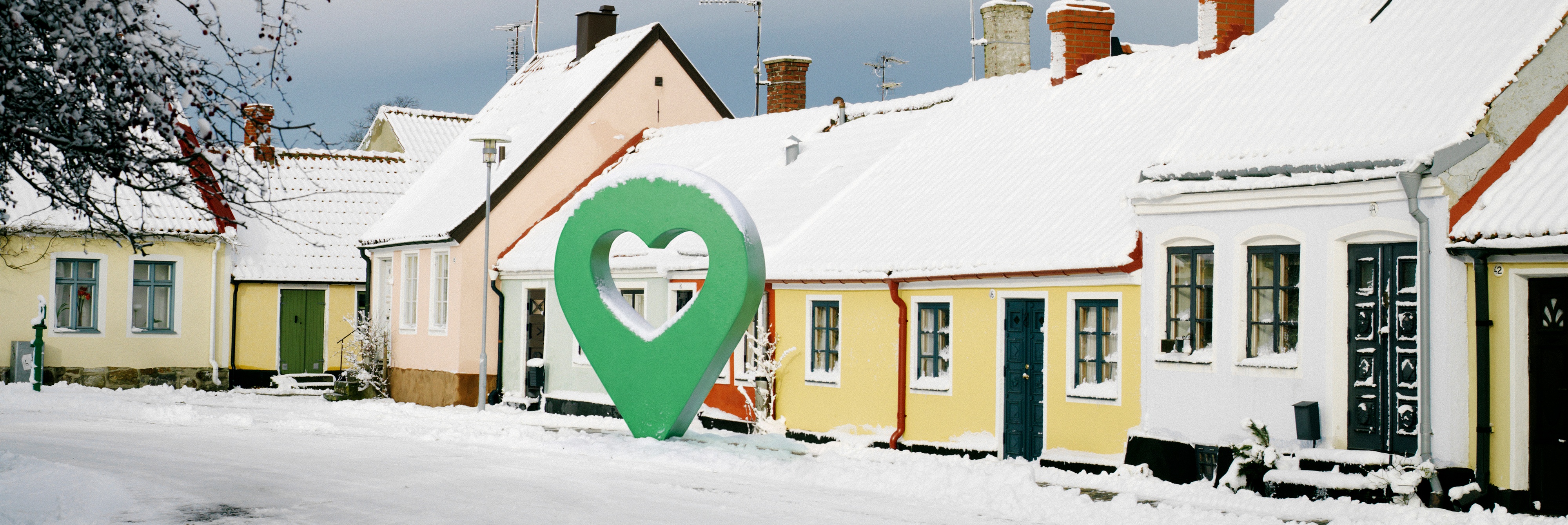 Snötäckt gata med pittoreska hus och en grön markörformad symbol i mitten.