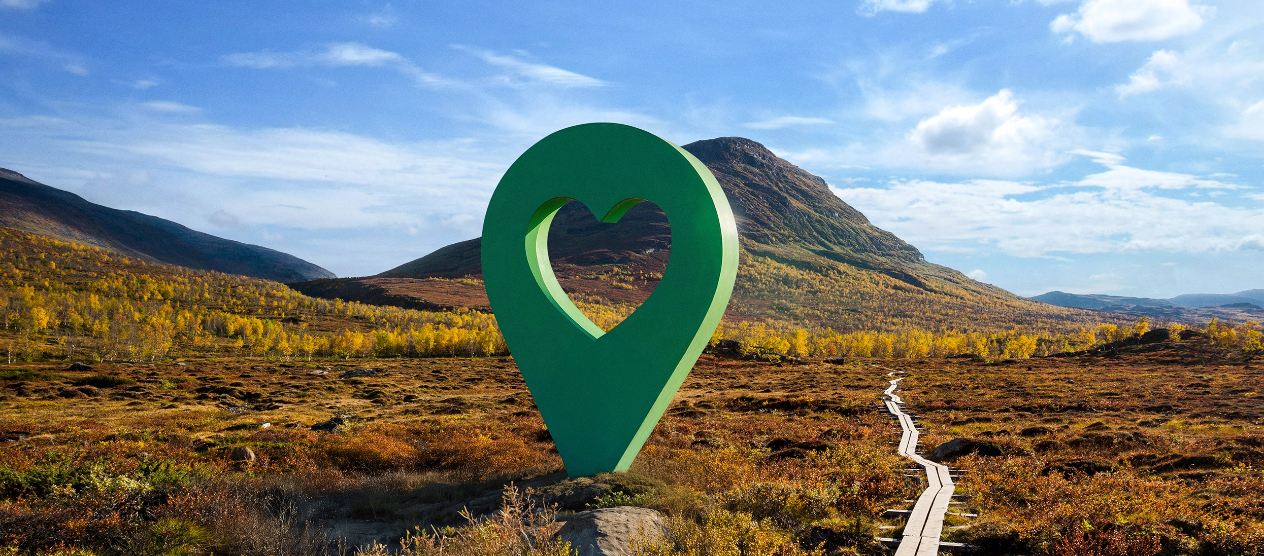 Bild av Lyckplatsen med en stor grön hjärtformad platsmarkering i ett vackert landskap under blå himmel.