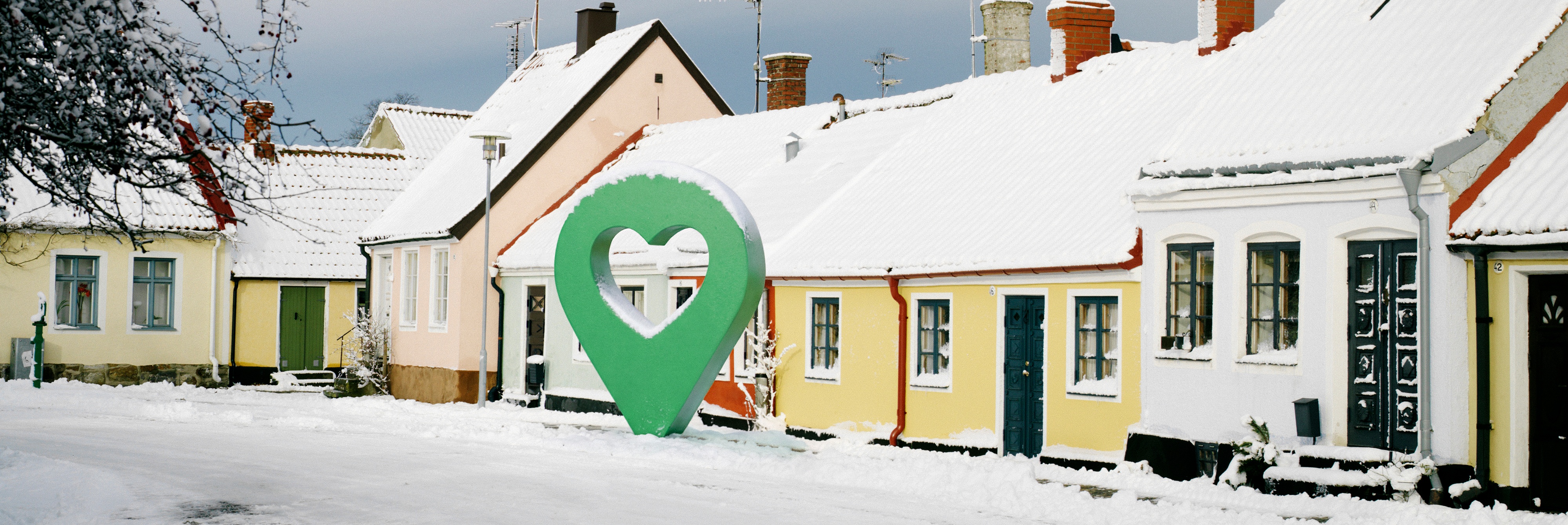Snötäckt gata med pittoreska hus och en grön markörformad symbol i mitten.