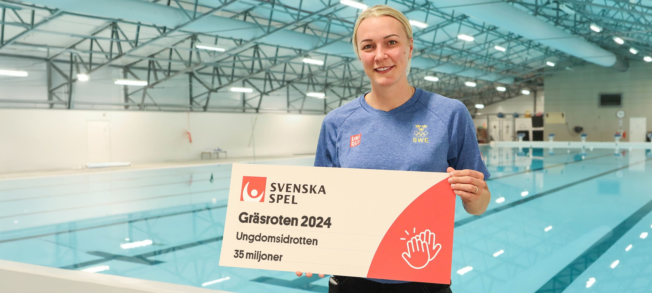 Sara Sjöström vid en pool som håller en check för Gräsroten 2024.