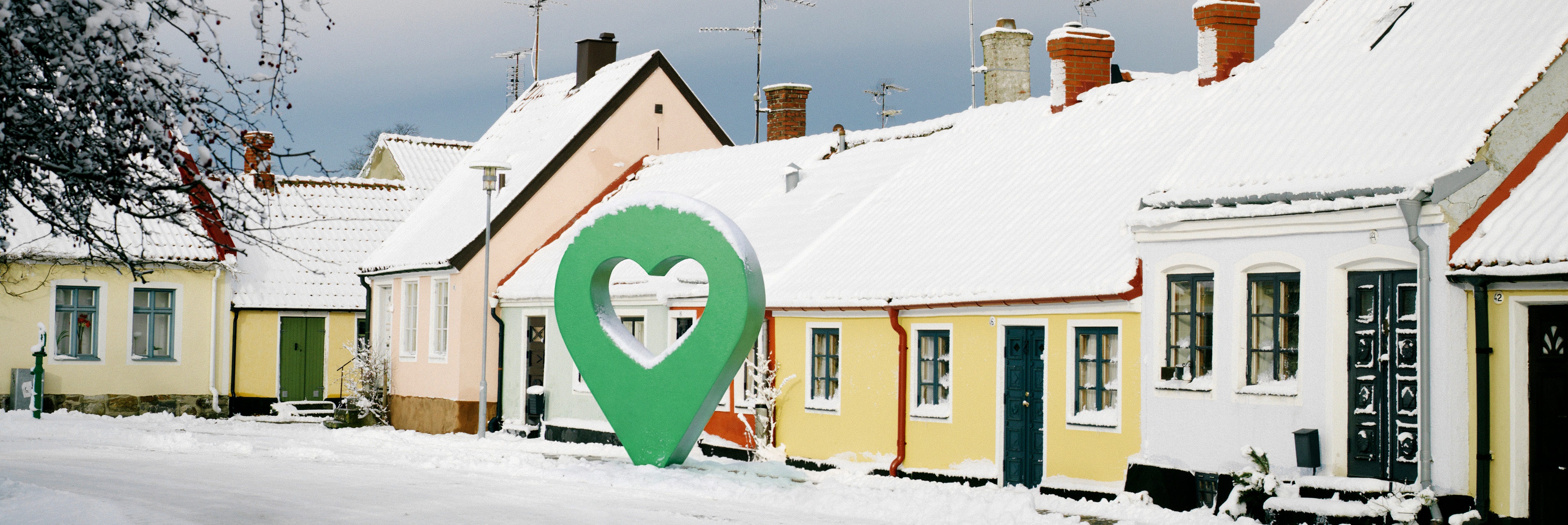 Snötäckt gata med pittoreska hus och en grön markörformad symbol i mitten.