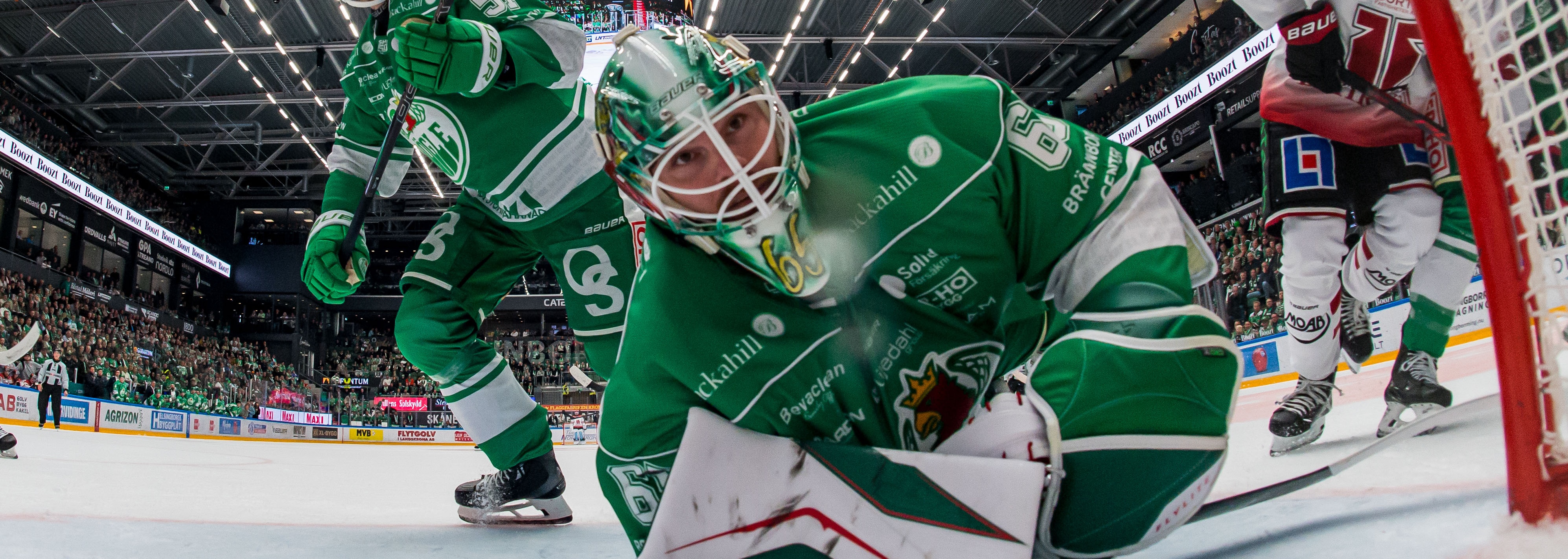 Hockeyspelare i gröna dräkter i en actionfylld match framför målet.