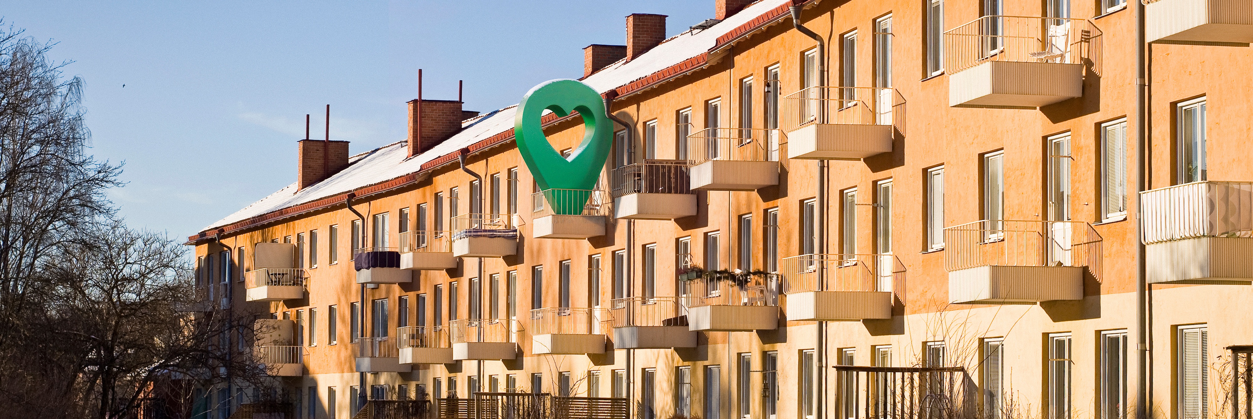 Lägenhetshus i vintermiljö med snöklädd mark och klarblå himmel.