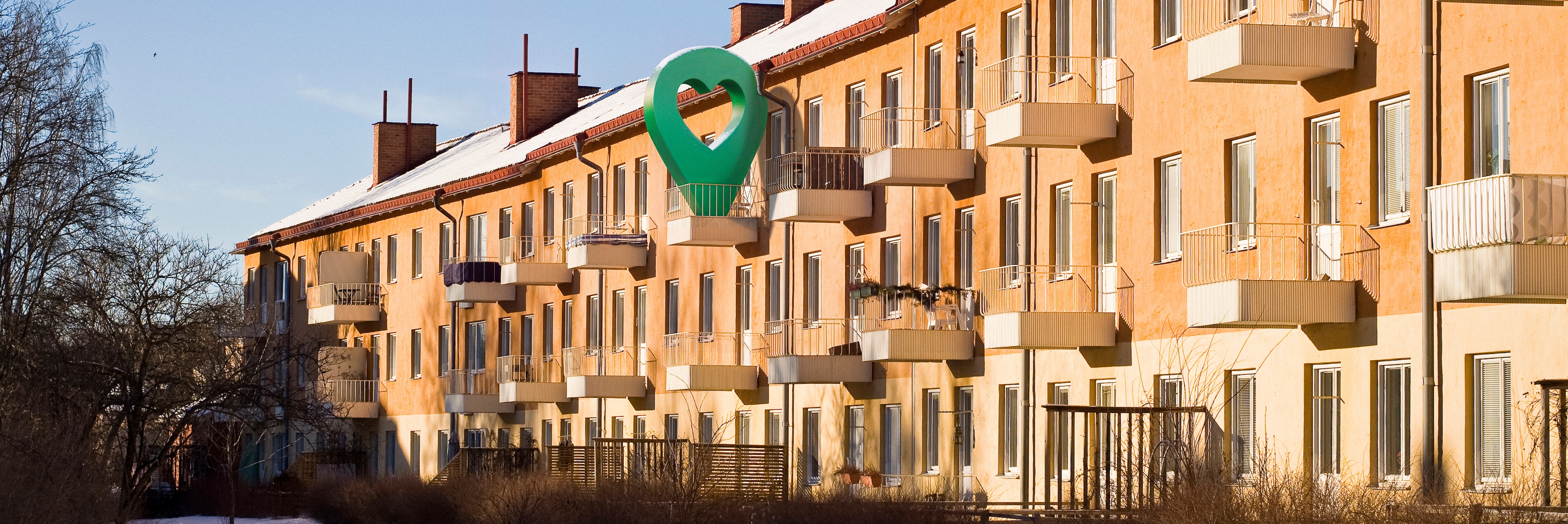Lägenhetshus i vintermiljö med snöklädd mark och klarblå himmel.