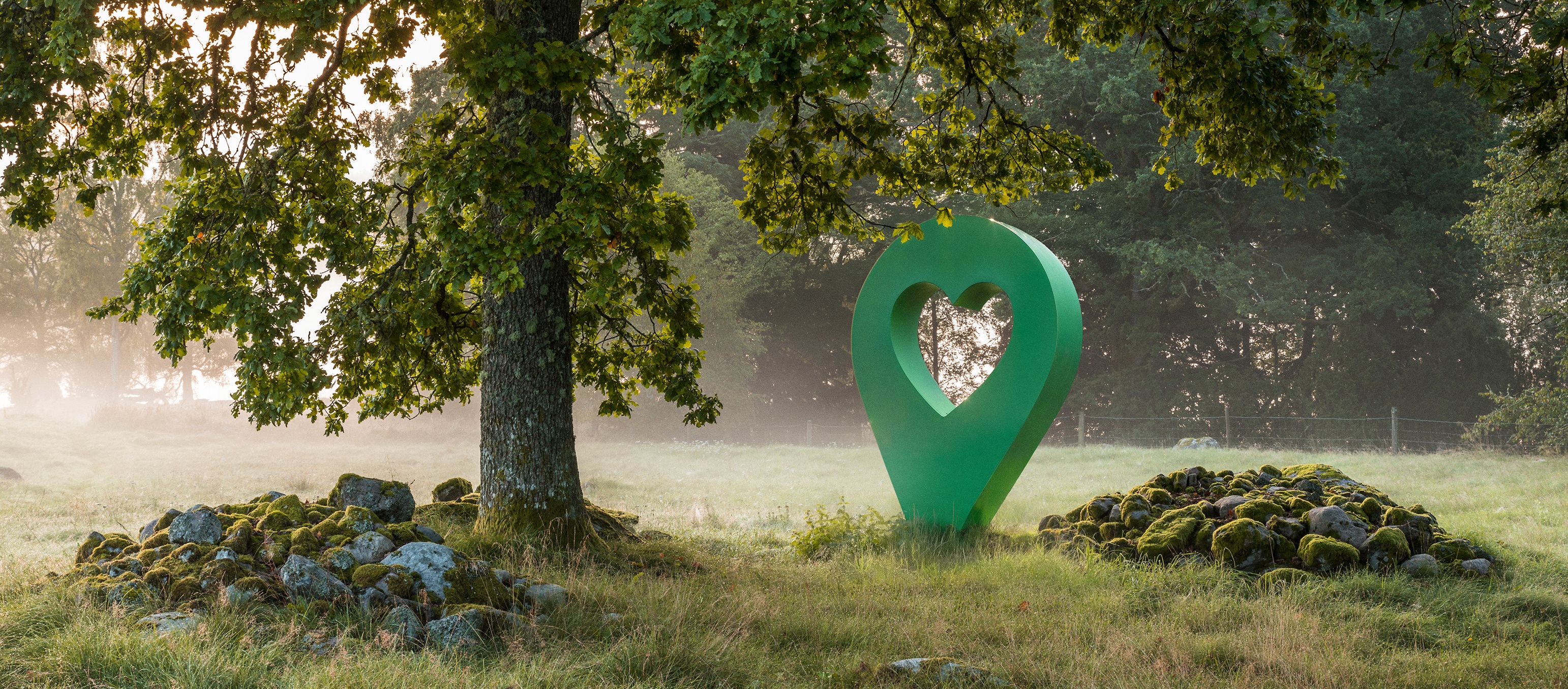 Grön lyckplats-symbol med hjärta mitt i en skog. Symbolen står nära ett träd och en stenig plats.