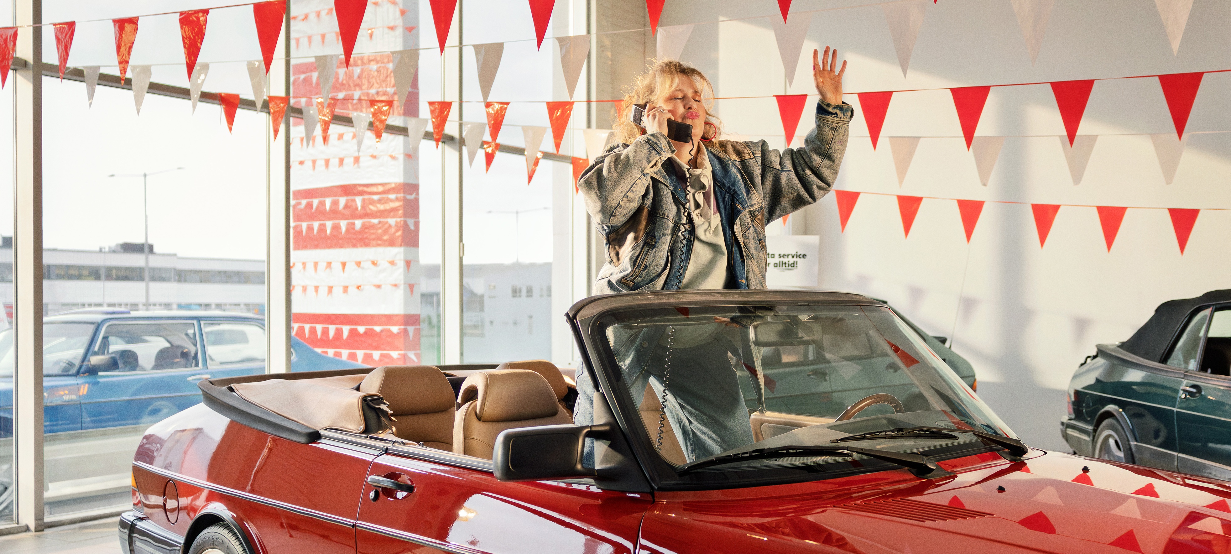 En person firar i en bilhall med en röd cabriolet och triangelformade flaggor hängande ovanför.